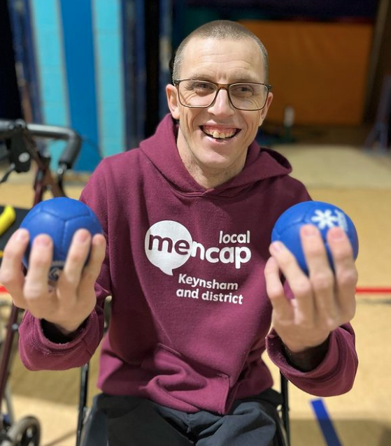 Paul sitting down holding 2 boccia balls March 2023